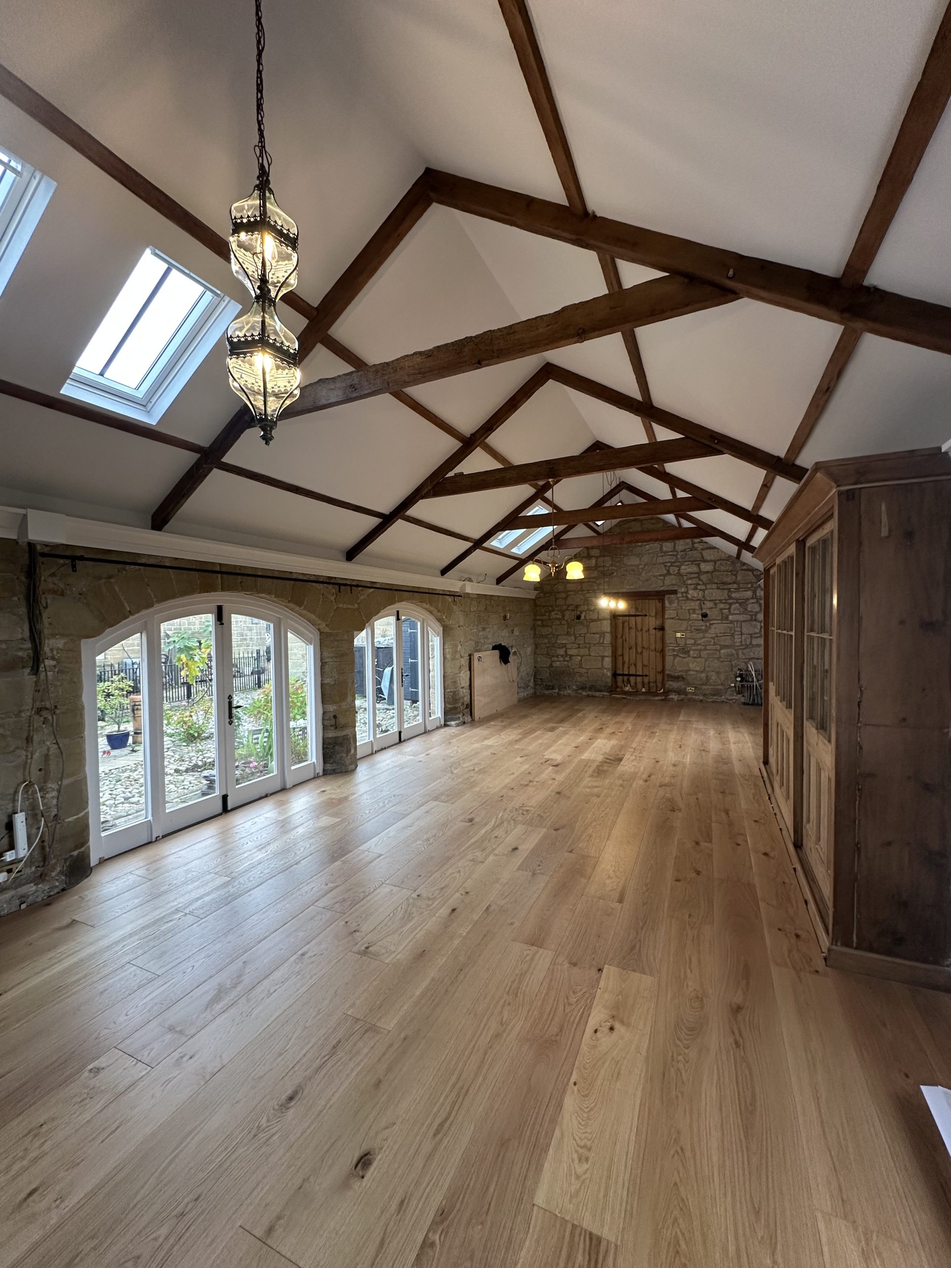 Wide plank oak flooring installed in a stone and timber-beamed room