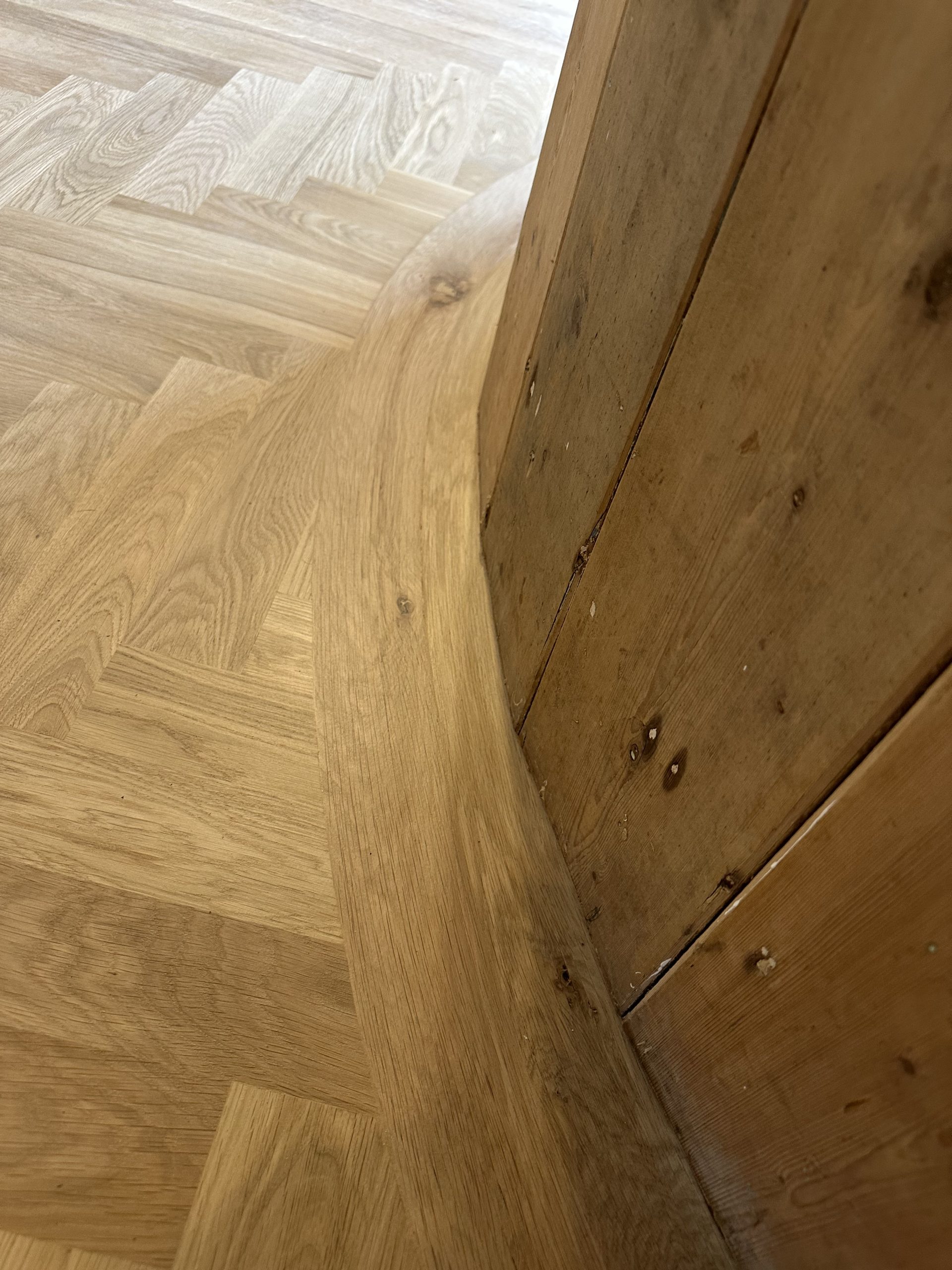 Bespoke Curved Oak Herringbone Border – Seahouses Bespoke curved oak flooring border following a timber-panelled wall in Seahouses, Northumberland
