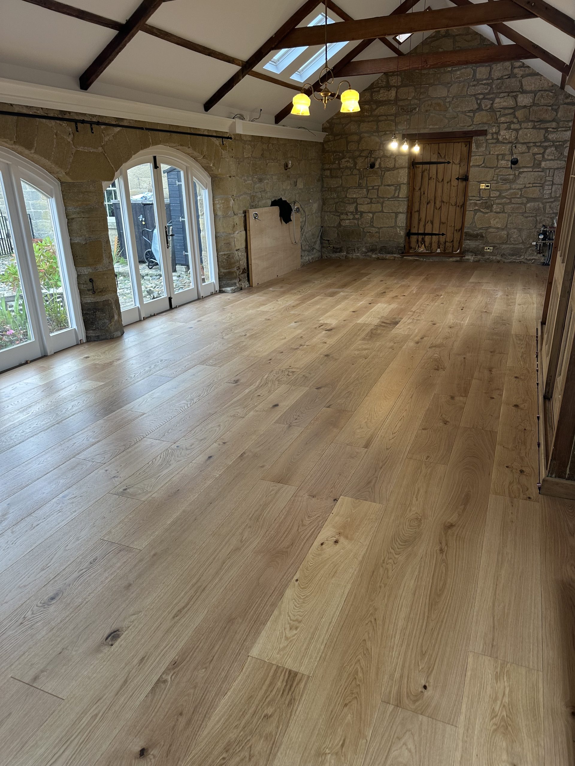 Wide engineered oak plank flooring beside exposed stone walls and arched doors in High Buston