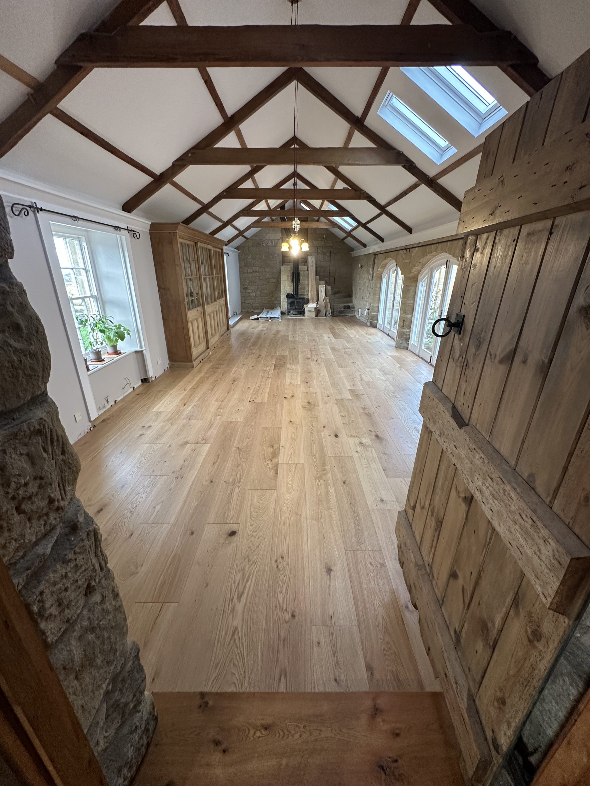 Wide engineered oak flooring installed in a spacious living room with exposed timber beams in High Buston